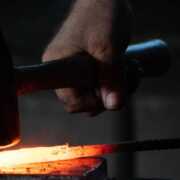 man pounding hammer on hot iron rod