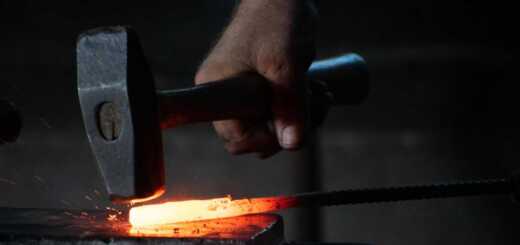 man pounding hammer on hot iron rod