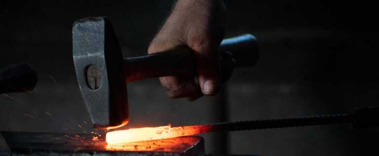 man pounding hammer on hot iron rod